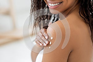 Mousturising Skin. Smiling Black Female Applying Nourishing Body Lotion, Closeup Shot