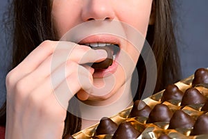 Mouth of woman is eating chocolate candies from box, closeup view.