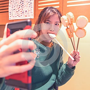 Mouthful Woman holding Four sticks of Sendai Famous Fish Tofu and taking selfie with her mobile phone