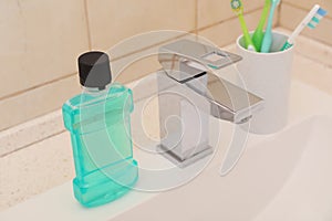 Mouthwash and holder with toothbrushes on sink in bathroom