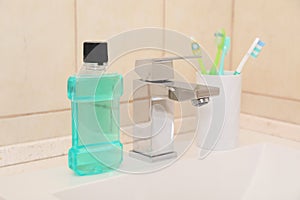 Mouthwash and holder with toothbrushes on sink in bathroom