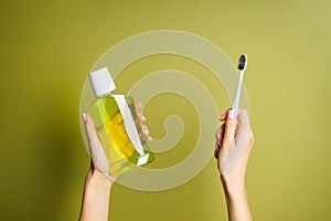 Mouthwash and toothbrush in the hands of a young woman on a green background. View from above. Morning concept