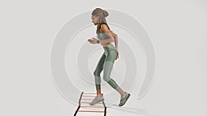 Move forward. Full length shot of young sportive mixed race woman in sportswear training on agility ladder drill