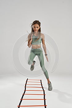 Move on. Full length shot of young sporty mixed race fitness woman in sportswear training on agility ladder drill