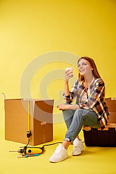 Move. Woman drinking coffee sitting on a tool box. Studio