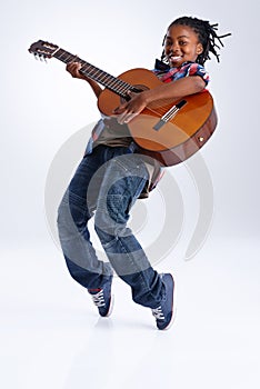 Moved by the music. A happy young African-American boy playing a guitar while balancing on his toes.