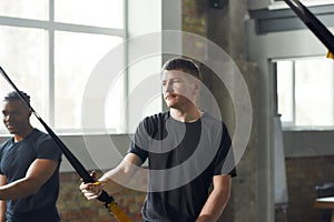 Movement Revolution. Portrait of caucasian man doing fitness TRX training exercises at industrial gym. Push-up, group