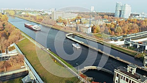 The movement of ships and barges along the canal through the river gateway in autumn sunny day.