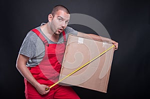 Mover guy holding box measuring with tape looking surprised