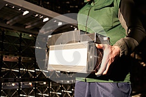 Mover holding bitcoin ASIC miner in warehouse. Worker with ASIC mining equipment on stand racks for mining