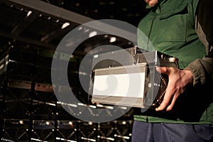 Mover holding bitcoin ASIC miner in warehouse. Worker with ASIC mining equipment on stand racks for mining