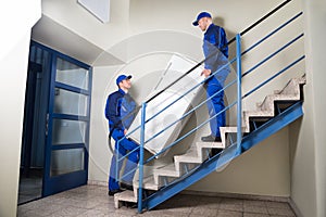 Movers Carrying Refrigerator On Steps At Home