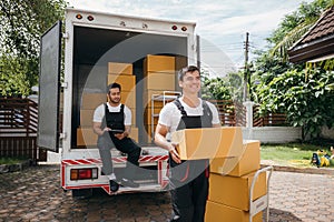 Movers unload boxes from a truck outdoors. Delivery service workers cooperate in