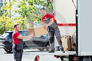 Movers Unloading A Moving Van And Passing A Cardboard Box