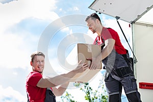 Movers Unloading A Moving Van And Passing A Cardboard Box