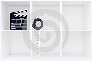 Movie clapper board and film reel on white bookshelf
