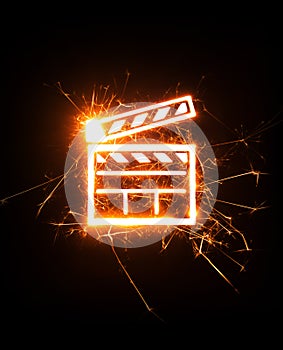 Movie clapper in glowing sparks on dark background.