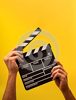 Movie clapperboard gripped by male hands on ayellow background