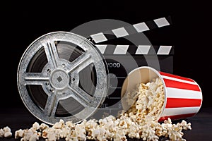 Movie film reel and film clapper with popcorn box on black