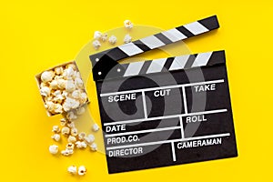 Movie premiere concept with clapperboard, popcorn on yellow background top view