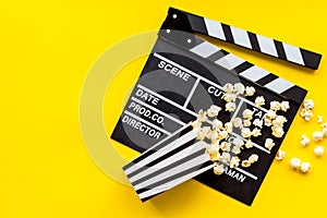 Movie premiere concept with clapperboard, popcorn on yellow background top view space for text