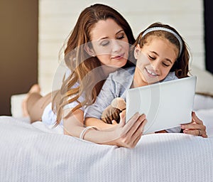 Movies are best enjoyed in bed. Full length shot of a mother and her daughter using a digital tablet.