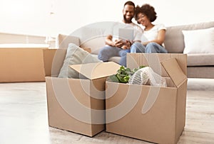 Moving Boxes Standing On Floor, Black Couple Using Tablet Indoor