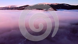 Moving clouds aerial view in the mountains. Drone flies high in purple sunset sky through the fluffy clouds in the fog
