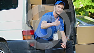 Moving company worker showing thumbs up, sitting in van full cardboard boxes