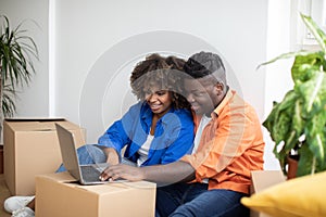 Moving Concept. Happy Black Couple Using Laptop In Their New Home