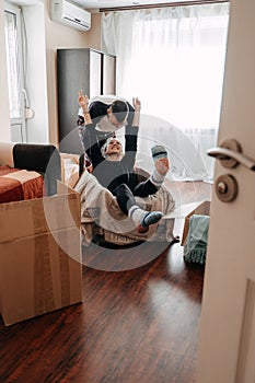 Moving day, Move Into New Home. Young happy couple, newlyweds family having fun in room with carton boxes with clothes