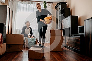 Moving day, Move Into New Home. Young happy couple, newlyweds family having fun in room with houseplant and carton boxes