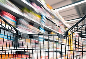 Moving empty black shopping cart with motion in the supermarket aisle, customer choosing product on market shelf store
