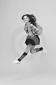 Moving with haste. Energetic child in midair yellow background. School girl in energetic jump. Back to school fashion