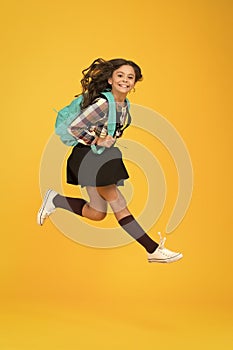 Moving with haste. Energetic child in midair yellow background. School girl in energetic jump. Back to school fashion