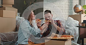 Moving in new home. Young happy family celebrate new apartment sitting on floor relaxing after unpacking, eating pizza.