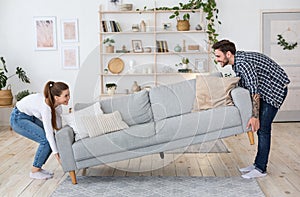 Moving or permutation furniture at home. Happy guy and girl raise sofa in interior of living room