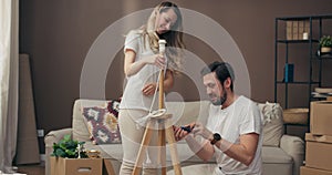 Moving in process delighted husband helping adorable young wife assembling new floor lamp in modern apertment. Cartom