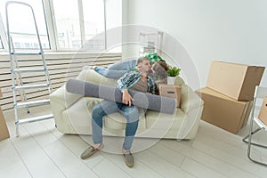 Moving, relocation and new home concept - young couple having fun on the couch surrounded with boxes