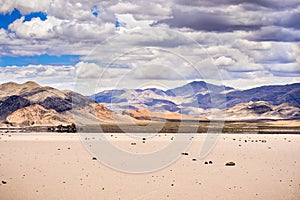 Moving rocks scattered around the surface of the Racetrack Playa; mountains and clouds scenery in the background; Death Valley