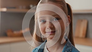 Moving shot close up little schoolgirl Caucasian child girl smiling looking at camera portrait at home kitchen cute 10s