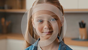 Moving shot close up little schoolgirl Caucasian child girl smiling looking at camera portrait at home kitchen cute 10s