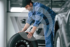 Moving the tire. Man in blue uniform is working in the car service