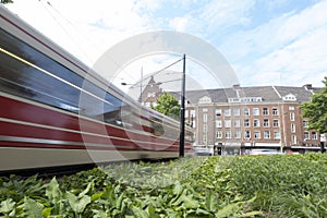 A moving tram at day, houses in background, blue sky, in long exposure. The Hague, the Netherlands