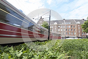 A moving tram at day, houses in background, blue sky, in long exposure. The Hague, the Netherlands