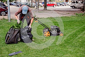 Mowing a household garden lawn with black bag of grass clippings