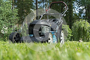 Mowing lawns. Lawn mower on green grass. Mower grass equipment. Mowing gardener care work tool close up view. Sunny day.