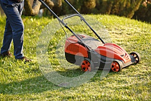 Mowing trimmer - worker cutting grass in green yard at sunset. Man with electric lawnmower, lawn mowing. Gardener