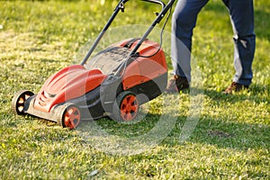 Mowing trimmer - worker cutting grass in green yard at sunset. Man with electric lawnmower, lawn mowing. Gardener