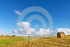 Mown field with round straw bales under a blue sky with clouds